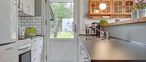 Una cocina moderna con muebles blancos, horno empotrado, lavaplatos y luces colgantes.