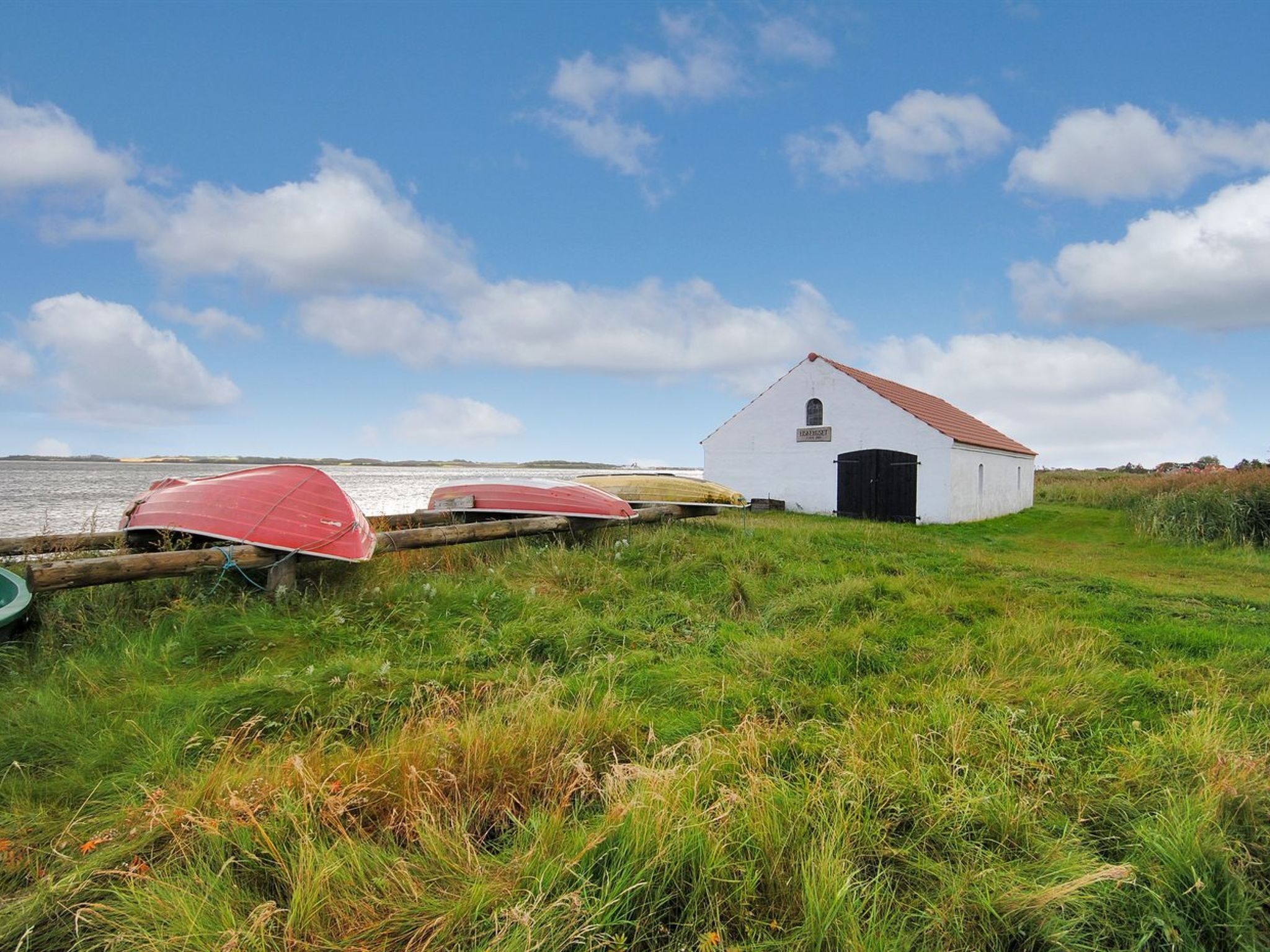 A white building with a red roof, surrounded by grass and a body of water.