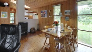 A wooden interior with a dining area, a black leather chair, and a kitchen in the background.