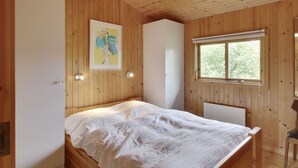 A wooden-paneled bedroom with a bed, a window, and a wall-mounted light fixture.
