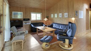 A wooden interior with a sofa, chairs, a TV, and a dining table.