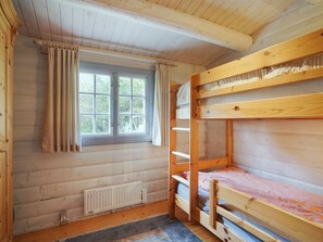 Una habitación de cabaña de madera con literas, una ventana con cortinas y un radiador.