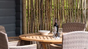 Een ronde houten tafel met rieten stoelen, een schaal, een fles en glazen.
