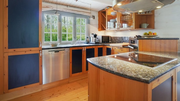 Een moderne keuken met houten kastjes, roestvrijstalen apparatuur en een groot raam met uitzicht op groen.