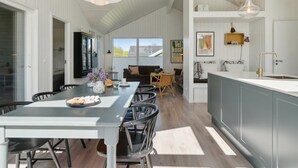 A modern kitchen with a dining area, featuring a large island, pendant lights, and a view to the outside.