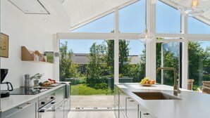A modern kitchen with large windows, a central island, and a view of a garden.