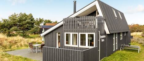 Eine moderne Holzhütte mit geneigtem Dach, einer Terrasse und einem Namensschild.