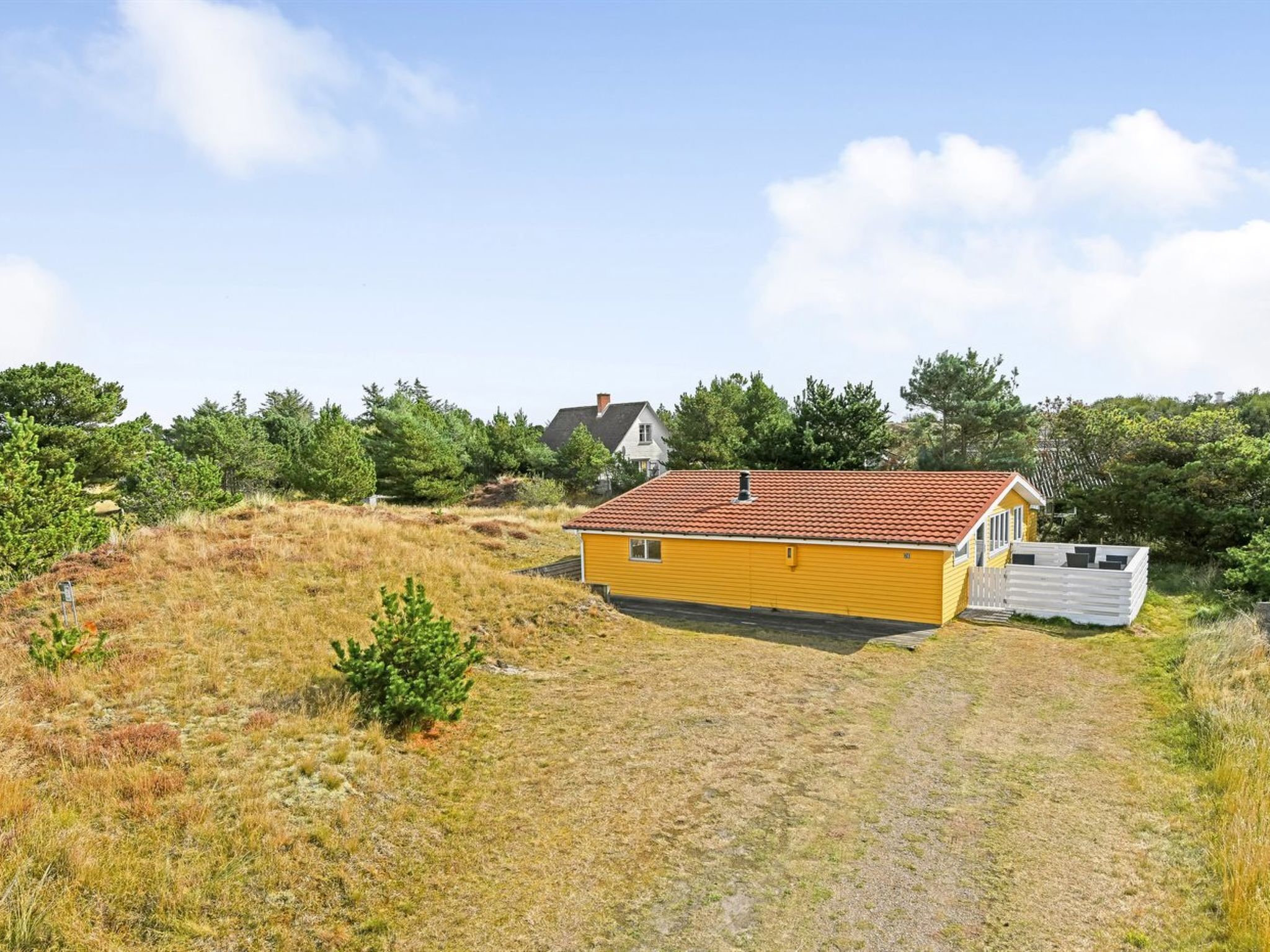 A yellow cabin with a red roof, surrounded by a grassy area and trees.