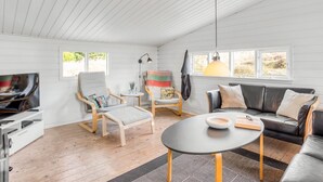 A spacious living room with a wooden floor, a black sofa, a wooden chair, a small round table, and a television. - "Heinke" - 2km from the sea by Interhome (Fanø)