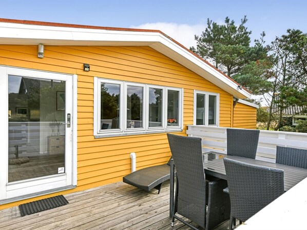 A yellow building with a deck, outdoor seating, and a sliding glass door.