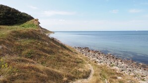 A coastal path with a rocky shoreline and a grassy hill.