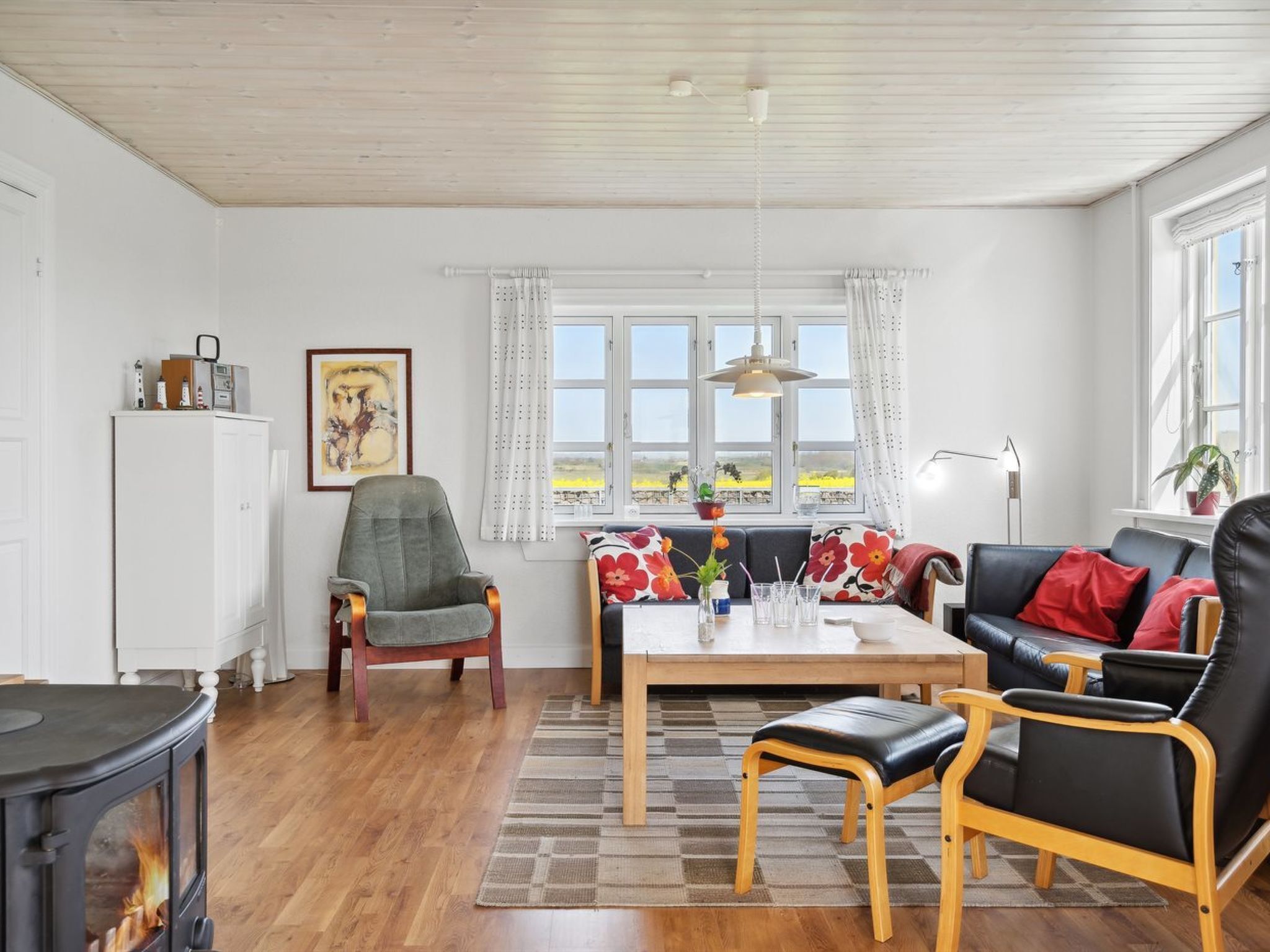 Un salon chaleureux avec un plancher en bois, un canapé, un fauteuil, une table ornée d’un vase et une cheminée.