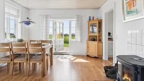 A spacious kitchen with a wood-burning stove, a dining area with wooden chairs and a table, and a view of the outdoors through open doors.