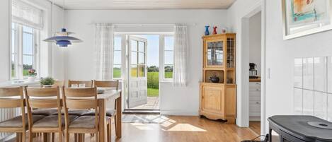 Una cocina amplia con estufa de leña, comedor con sillas y mesa de madera, y vistas al exterior a través de puertas abiertas.