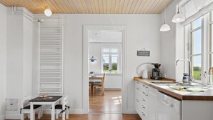 A bright kitchen with white cabinets, a wooden countertop, and a view of the outdoors through large windows.