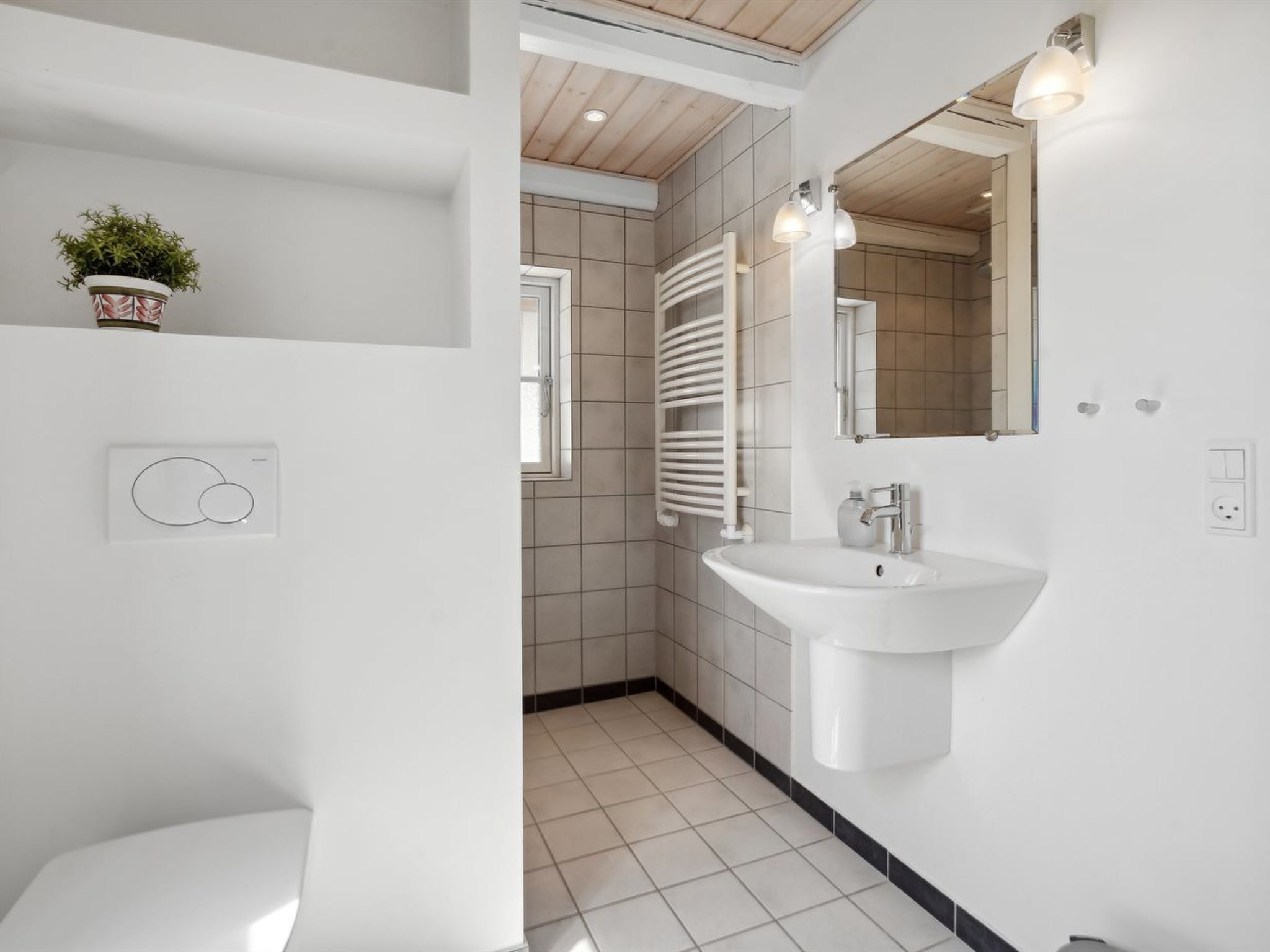 Uma casa de banho moderna com lavatório branco, espelho e suporte para toalhas.