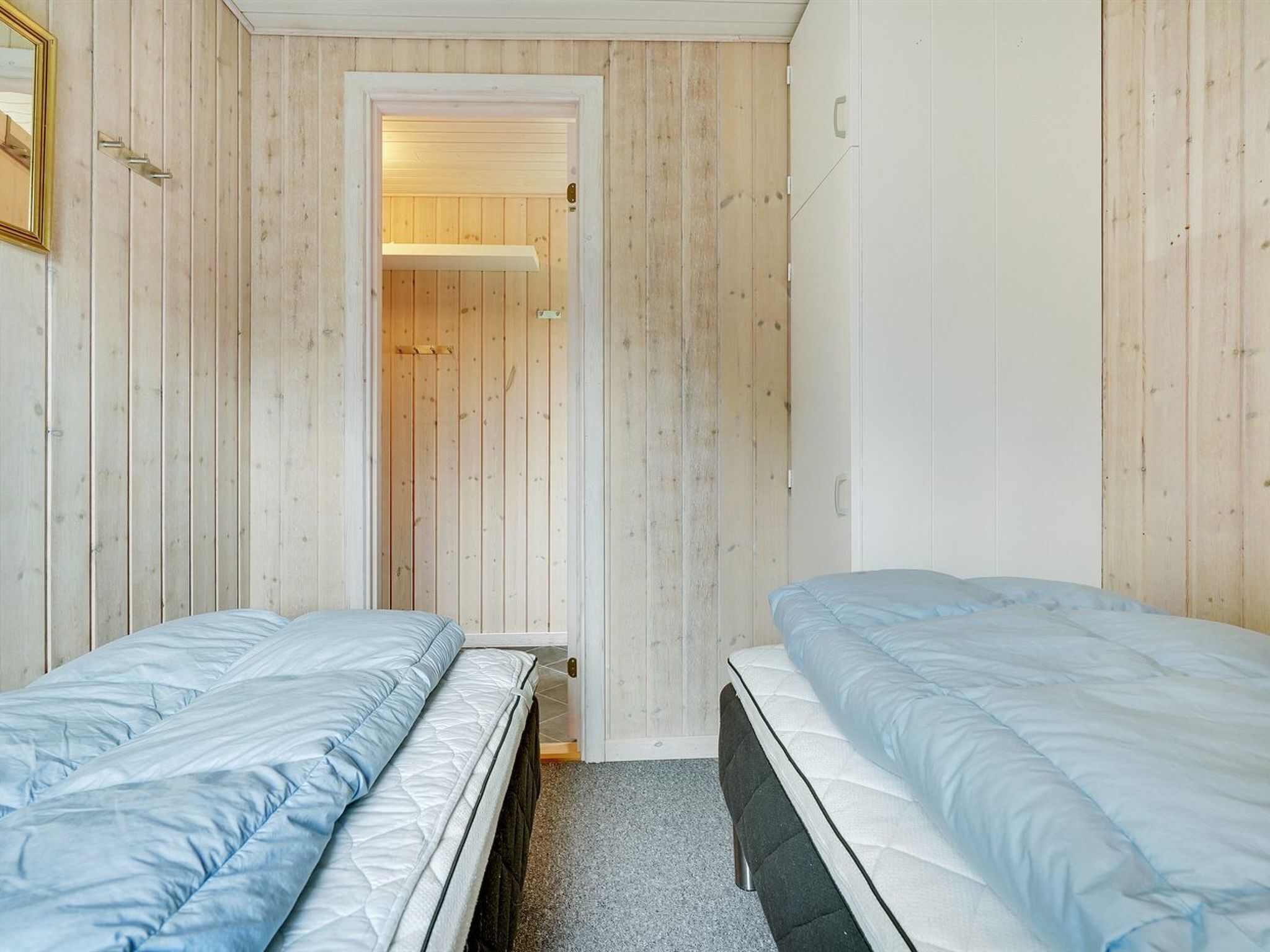 Ett rum med två sängar, träpanel på väggarna, en dörr som leder till ett badrum och en spegel på väggen till vänster.