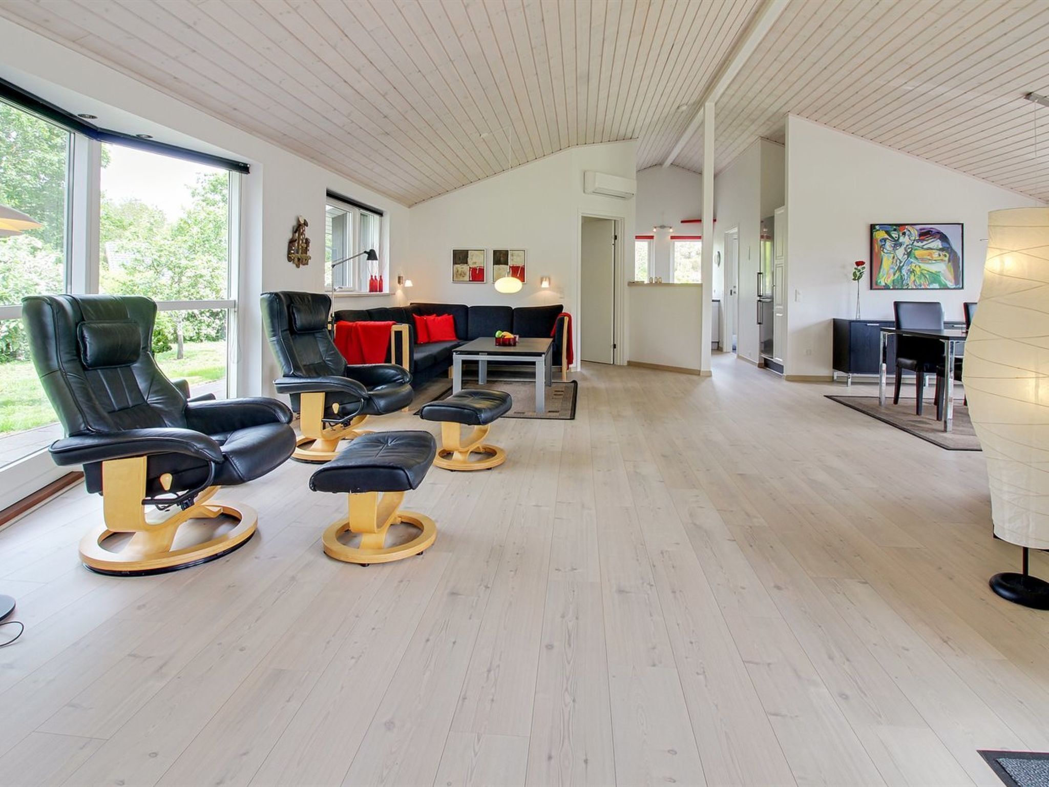 A modern room with a wooden ceiling, a black leather sofa, a dining table, and a large window.