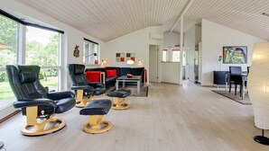 Ein modernes Zimmer mit Holzbalkendecke, einem schwarzen Ledersofa, einem Esstisch und einem großen Fenster.