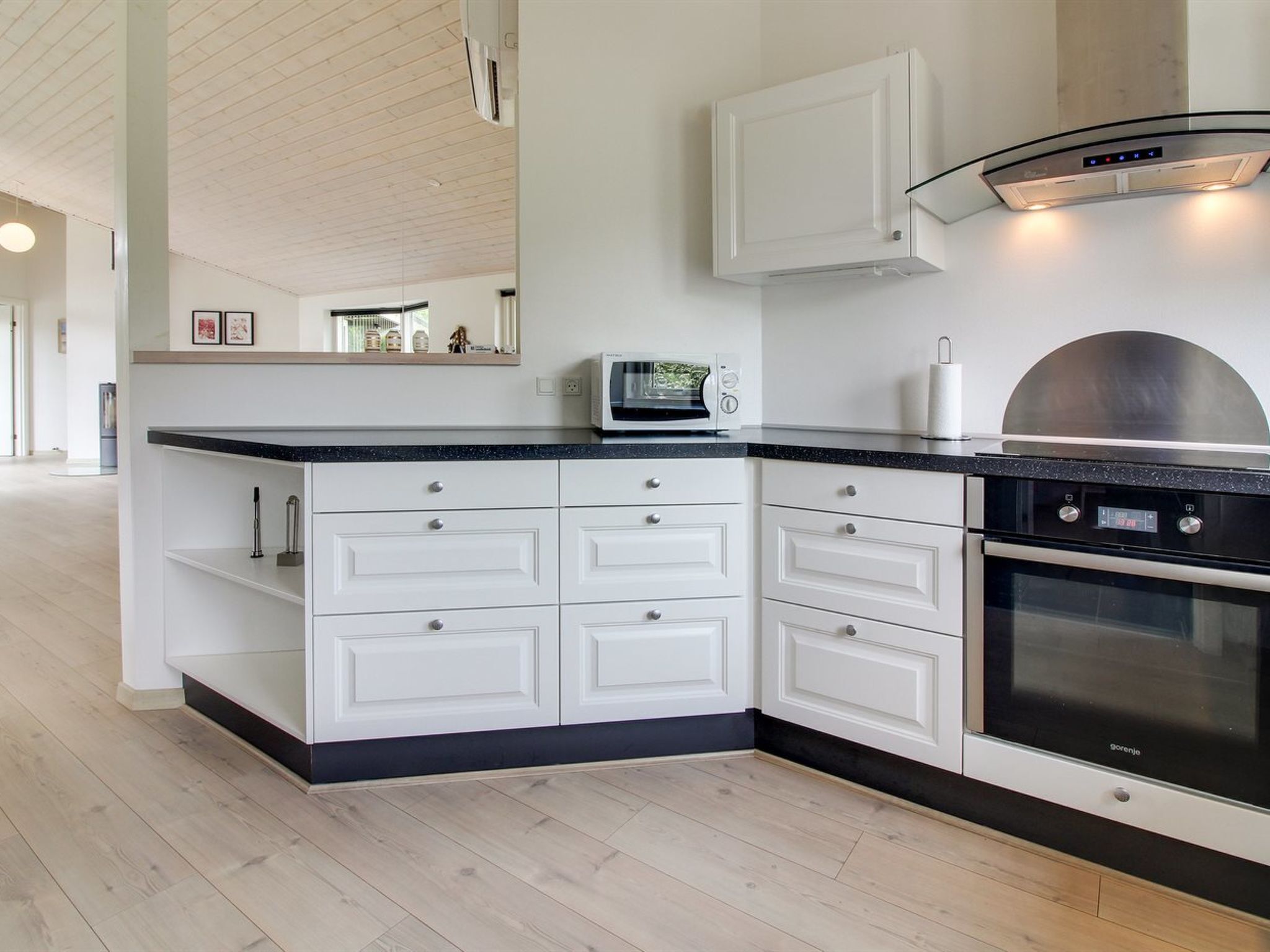 Una cocina moderna con armarios blancos, encimera negra, horno empotrado y microondas.