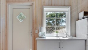 Une cuisine avec une porte blanche, une fenêtre donnant sur des arbres et une machine à café posée sur le plan de travail.