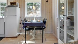 Une cuisine compacte avec un coin repas, des murs en bois, un réfrigérateur et un meuble vitré contenant de la vaisselle.
