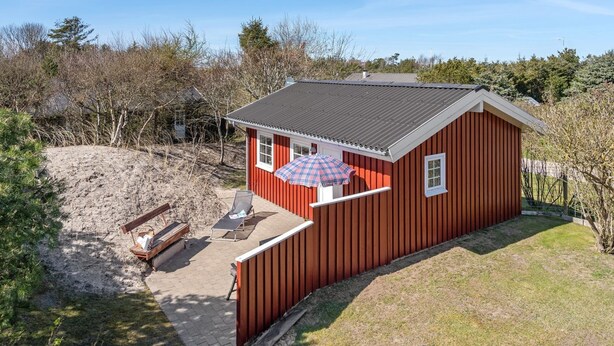 Une petite cabane en bois rouge avec un petit espace patio, un banc et une table avec une chaise.