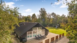 Et moderne hus med stor terrasse, swimmingpool og legeplads i baggrunden.
