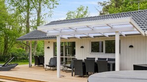 Eine überdachte Terrasse mit Esstisch und Stühlen, einem Grill und einem Holzboden.