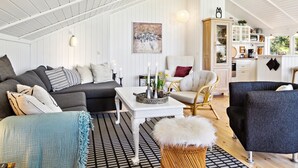 Ein gemütliches Wohnzimmer mit einer Couch, Sesseln, einem Couchtisch und einem Essbereich mit Schrank und Fenster.