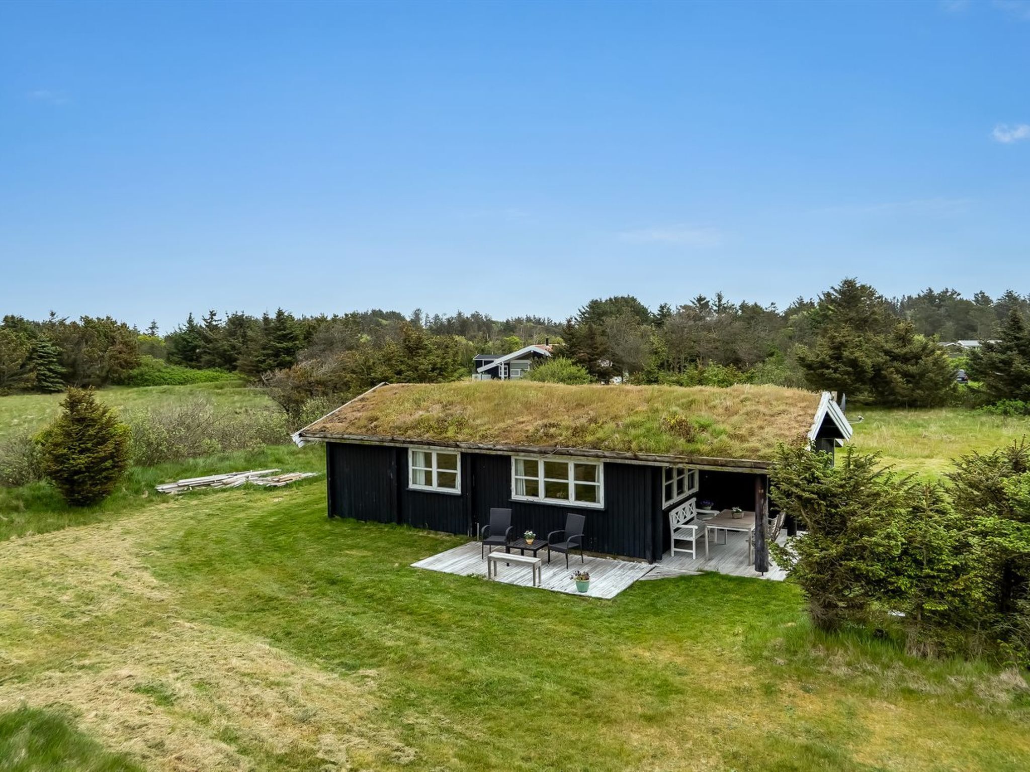 Eine schwarze Hütte mit Gründach, umgeben von einem grasbewachsen Feld und Bäumen.