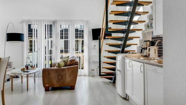 A modern kitchen with white cabinets, a wooden staircase, and a dining area with a sofa and table. - "Eleen" - 100m to the fjord by Interhome (Vestervig)