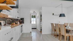A modern kitchen with white cabinets, a wooden countertop, and a dining area with wooden chairs and a table. - "Eleen" - 100m to the fjord by Interhome (Vestervig)
