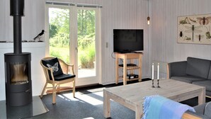 A modern living room with a wood-burning stove, a television on a wooden stand, a sofa, a coffee table, and a chair with a cushion. - "Kustaa" - 1km from the sea by Interhome (Humble)