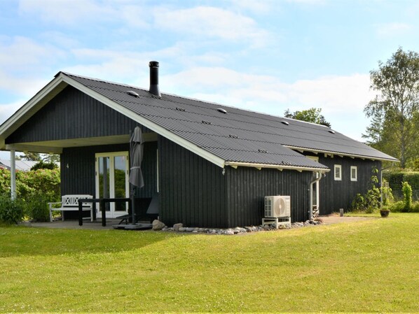 A black metal building with a sloped roof, a covered porch, and a small garden area.