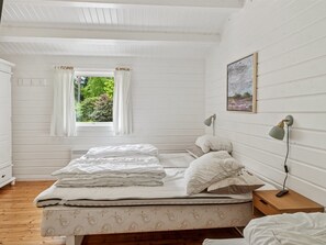 Un dormitorio con cama, mesita de noche, lámpara, ventana con cortinas y un cuadro en la pared.