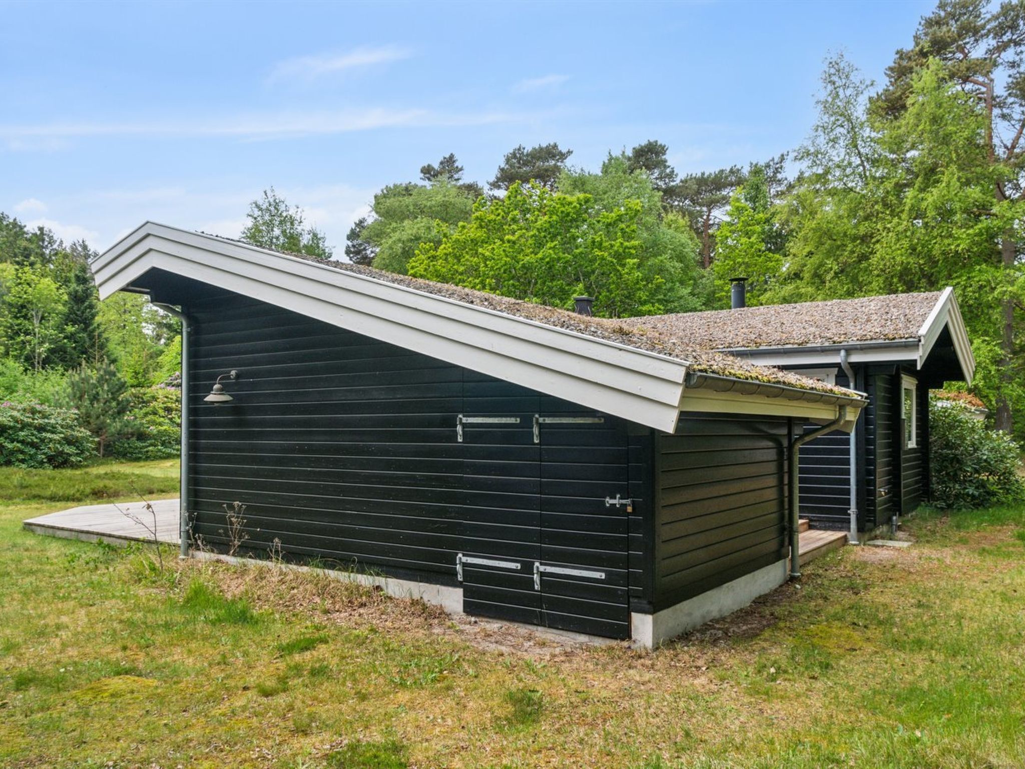 Un abri de jardin en métal noir, doté d’un toit en pente et d’une petite structure adjacente avec un toit à deux versants.