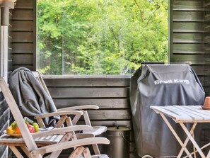 Una terraza de madera con una parrilla, una mesa y una silla con una chaqueta.