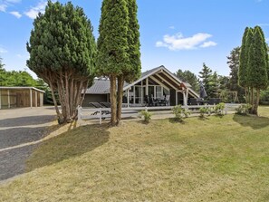 Una casa moderna con un porche cubierto, un parque infantil y un patio cercado.