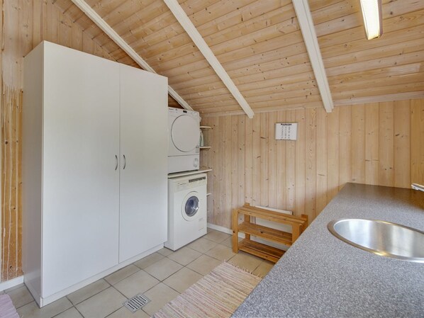 Una cocina compacta con paredes de madera, una lavadora, un taburete pequeño de madera y un lavabo.
