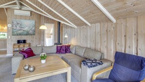 Een gezellige woonkamer met een houten plafond, een grijze bank, een blauwe fauteuil en een houten salontafel.