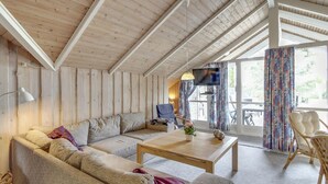 Een gezellige woonkamer met een houten plafond, een bank, een salontafel en een televisie.