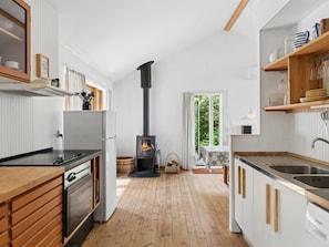 Eine moderne Küche mit Holzofen, weißen Schränken und Blick durch ein Fenster.