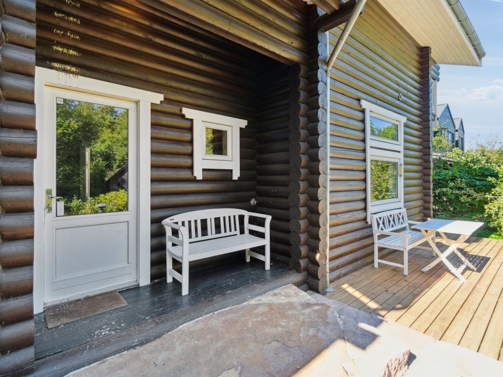 A log cabin with a porch, a bench, and a table.