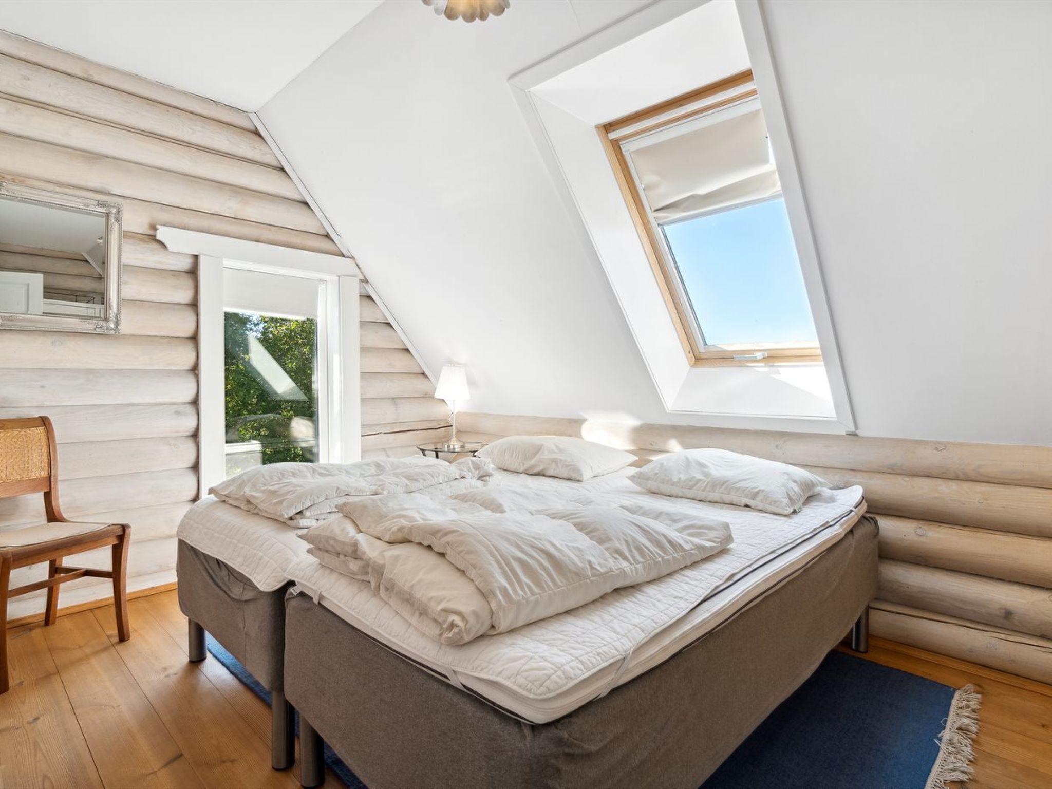 A bedroom with a sloped ceiling, a skylight, a bed, a chair, and a bedside table.