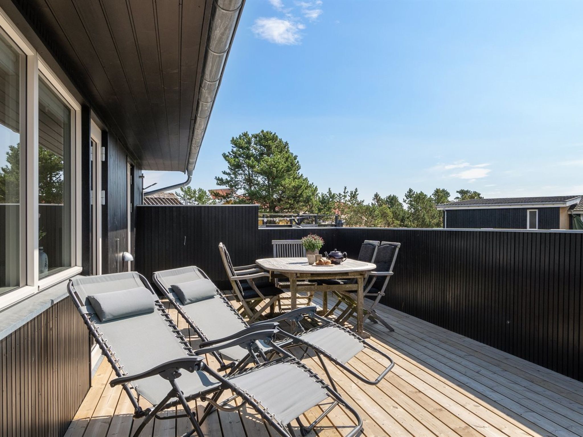A deck with lounge chairs and a table, surrounded by a wooden deck and a dark fence.