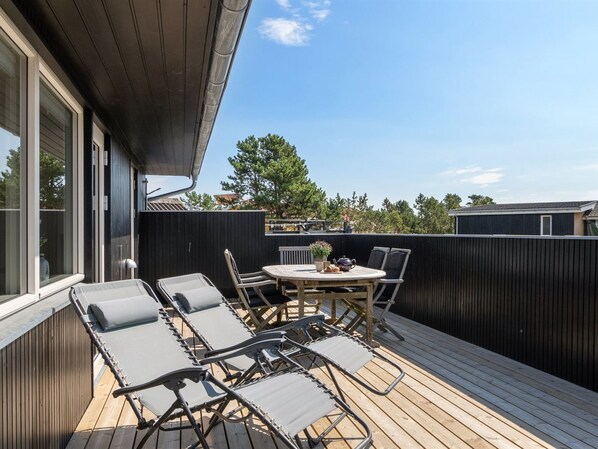 A deck with lounge chairs and a table, surrounded by a wooden deck and a dark fence.