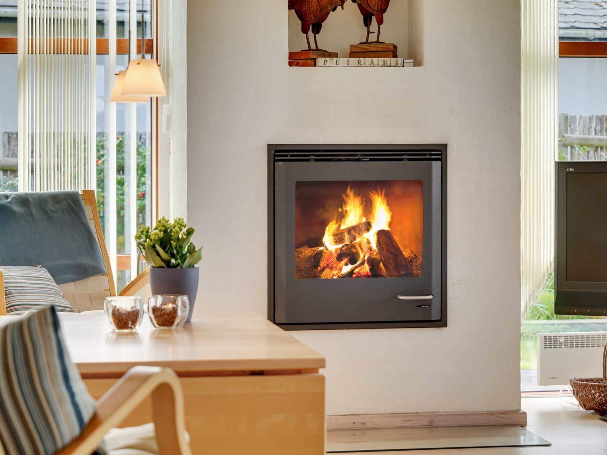 A modern living room with a fireplace, a sofa, a coffee table, and a view of the outdoors.