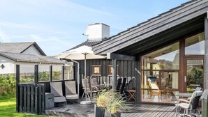 Eine moderne Außenpatio mit Holzterrasse, Sitzgelegenheiten im Freien und einer großen Glasdoor, die zum Innenbereich führt.