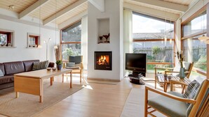 Ein geräumiges Wohnzimmer mit Kamin, großen Fenstern und einer gemütlichen Sitzecke.